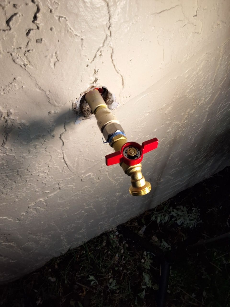 Red-handled shutoff valve on a pipe protruding from a cracked ceiling.