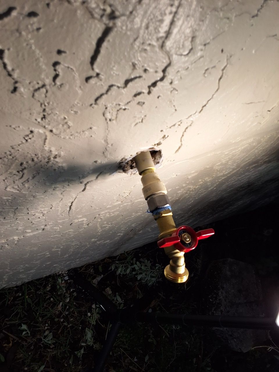 Outdoor water spigot with red valve mounted under a textured concrete overhang at night