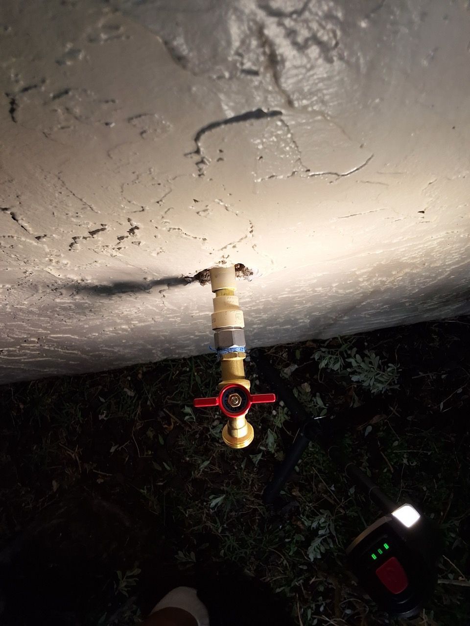A ceiling-mounted pipe valve with a red handle, photographed at night with trees and a light in the background