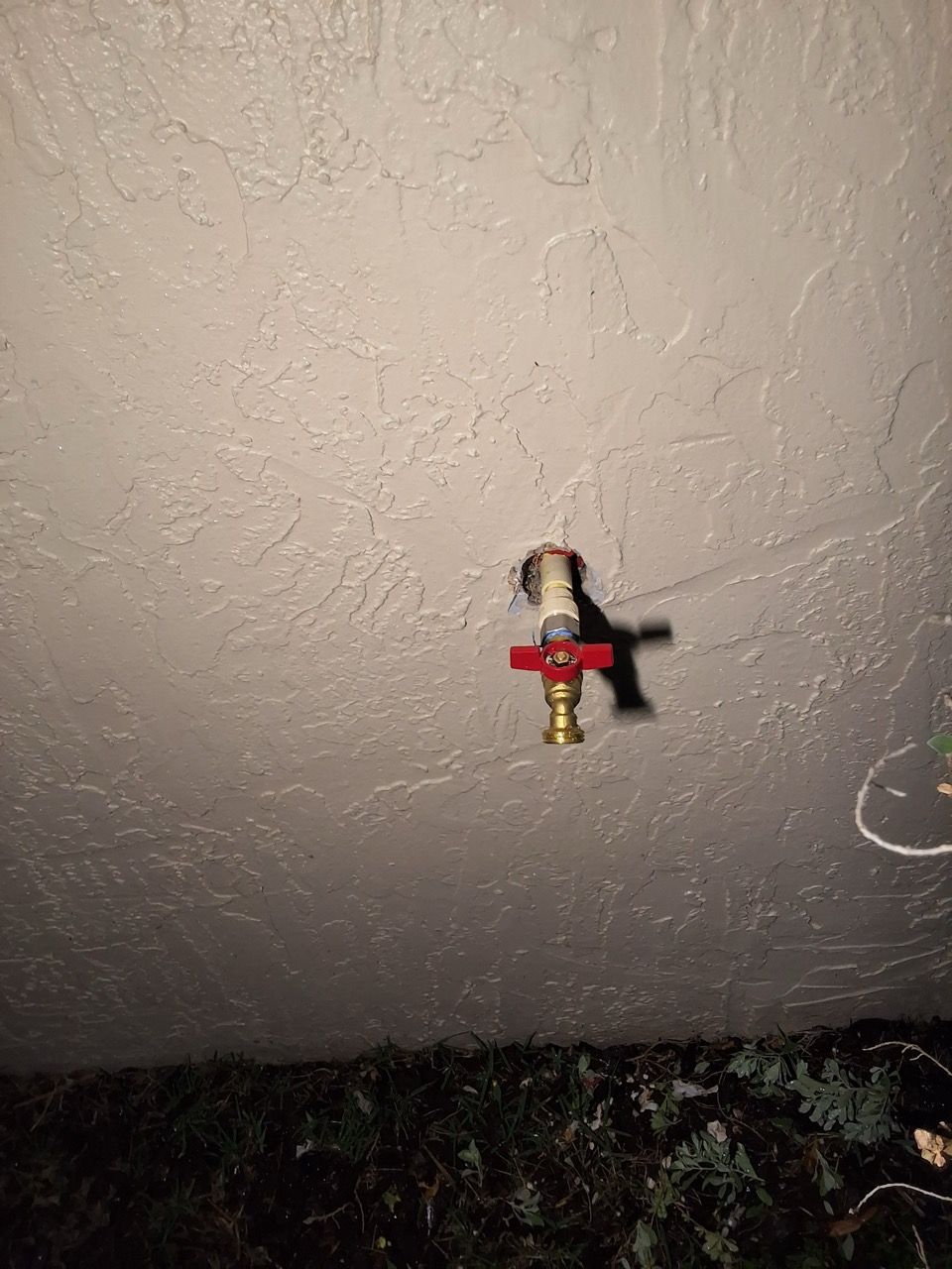 Small brass sprinkler valve on a textured ceiling, with a red handle against a gray background.