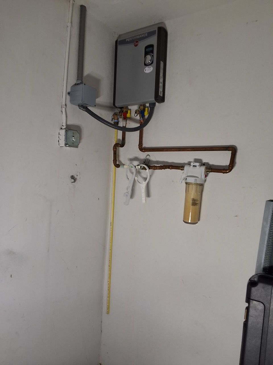 Wall-mounted utility meter and pipes with a filter canister on a white wall.