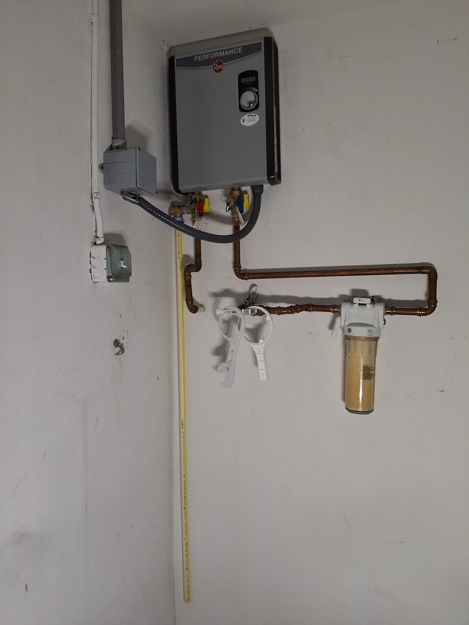 Wall-mounted utility equipment with pipes, valves, and an electrical control box on a white wall.