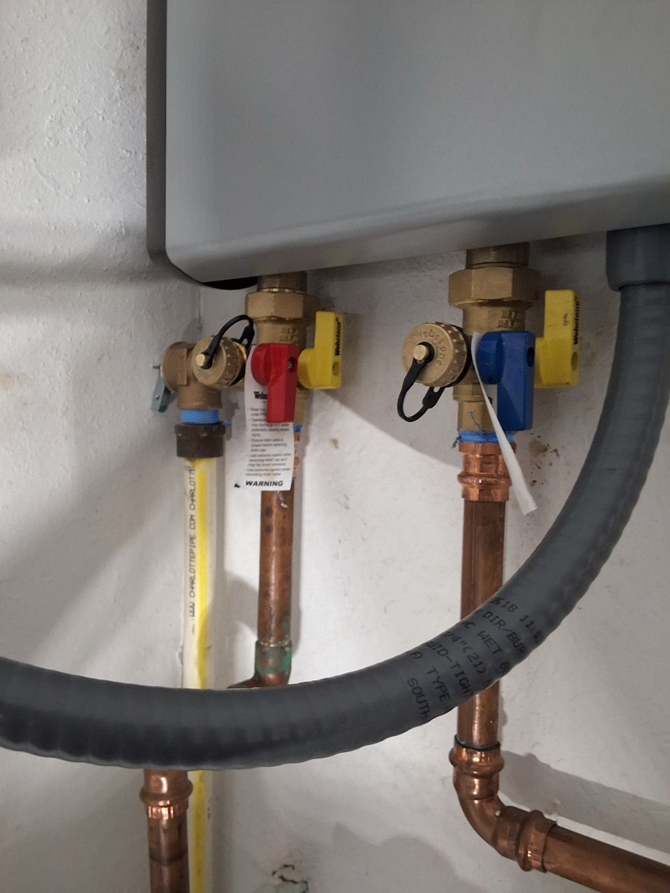 Two copper pipes with yellow shutoff valves and a black hose beneath a gray tank.