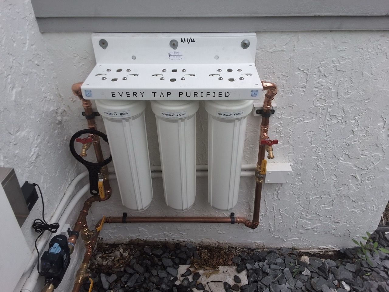 Three-canister water filtration system mounted outdoors against a wall with copper pipes.