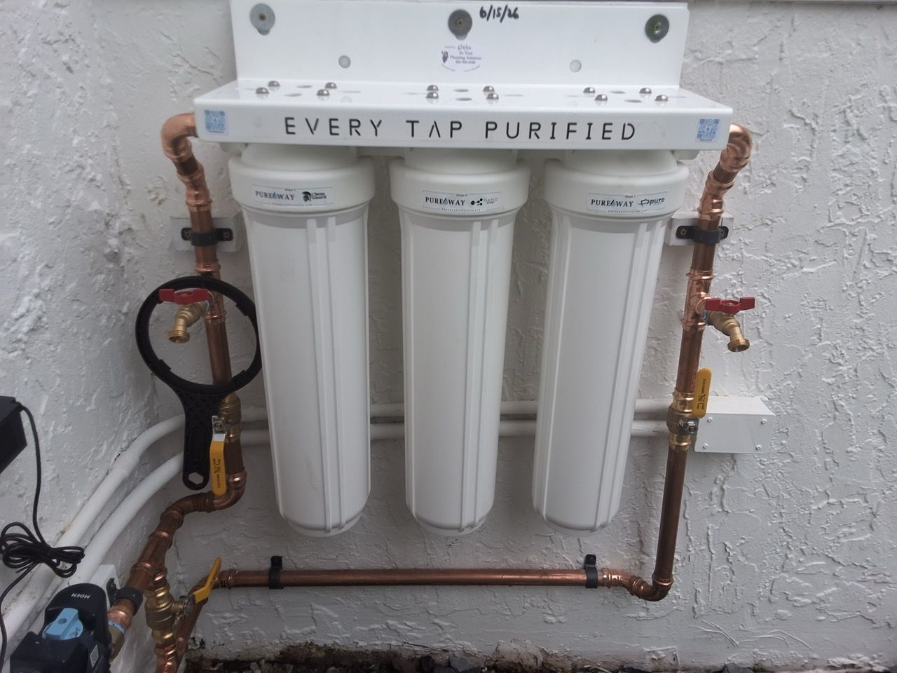 Three-stage water filter system mounted on a wall with copper pipes and valves.