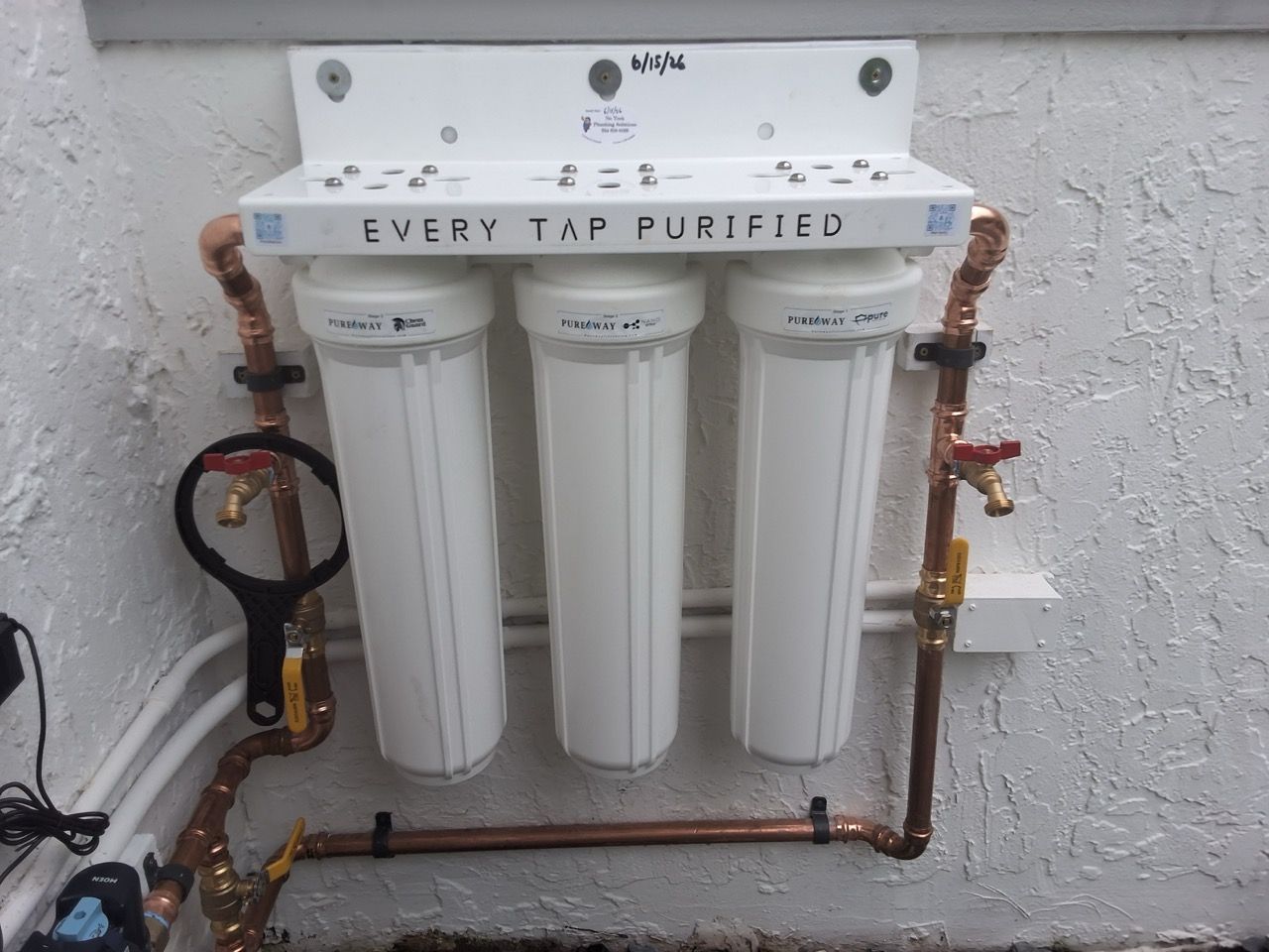 Whole-house water filtration system with three white canister filters and copper piping against a wall