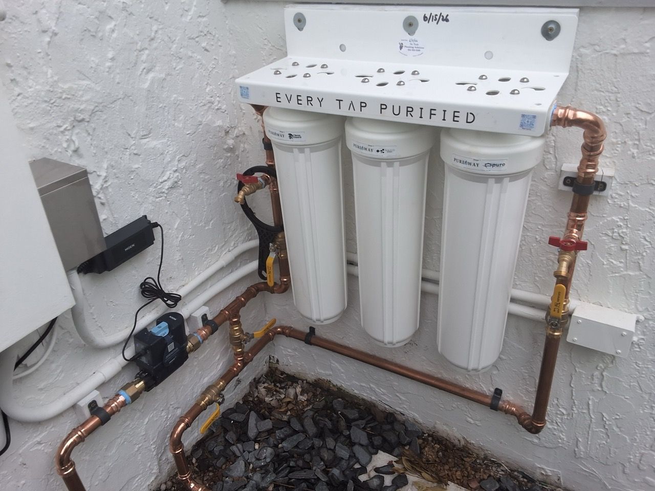 Water filtration system with three white filter canisters and copper piping on an exterior wall.