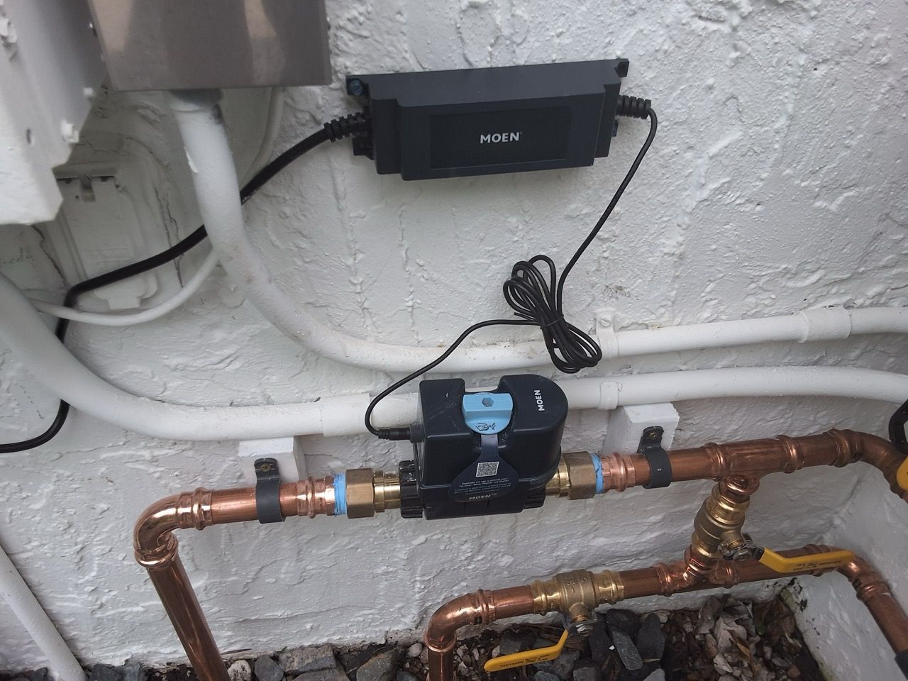 Copper pipes with a blue shutoff valve and black control box on a white wall.