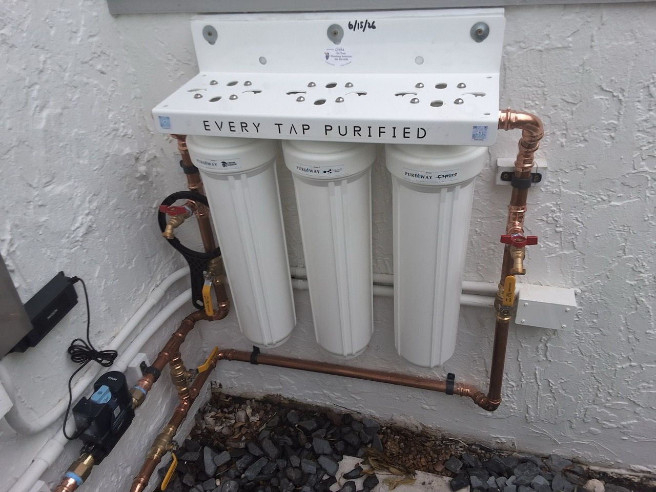 Under-sink water filtration system with three white filter cartridges and visible copper piping