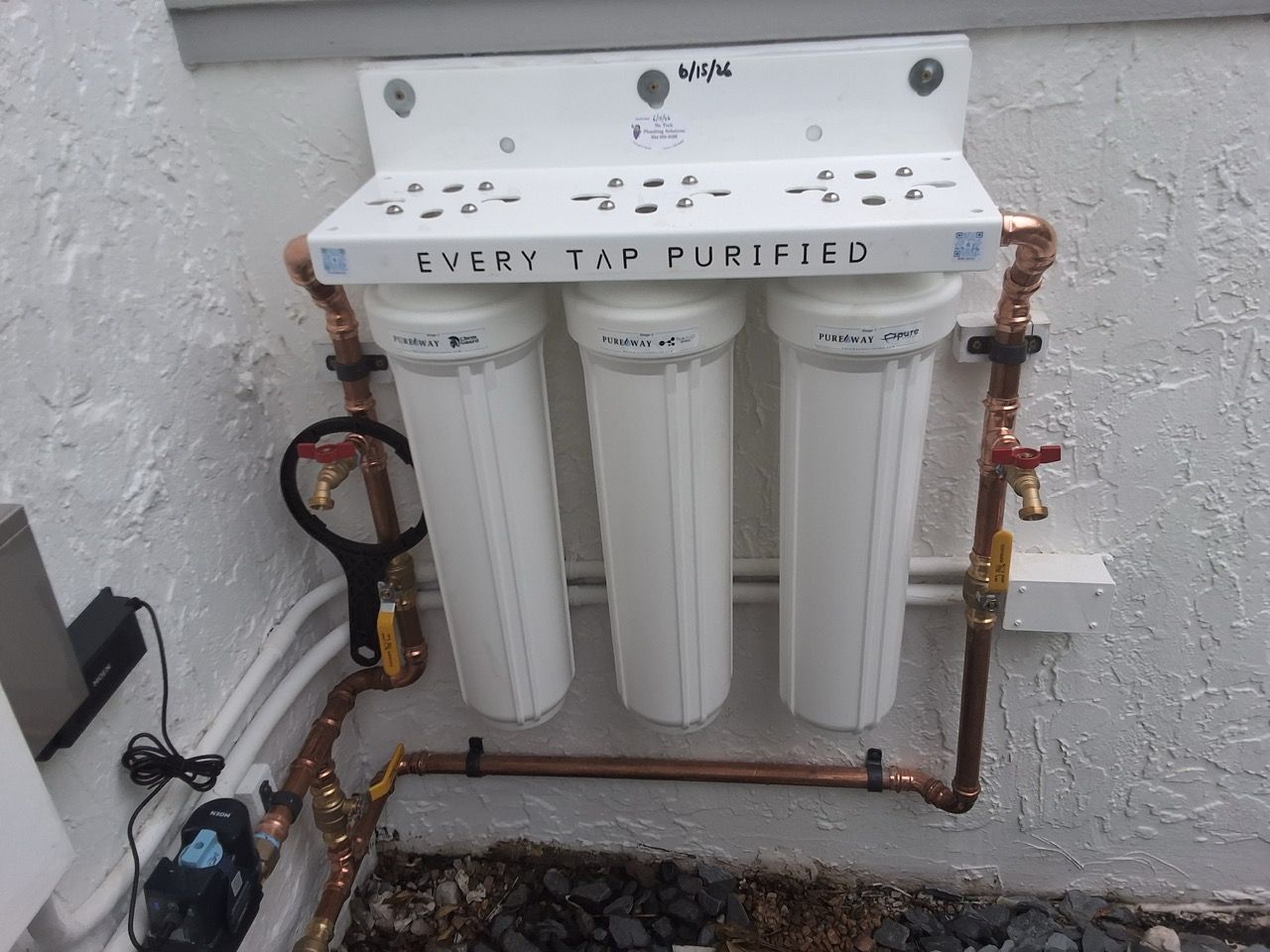 Wall-mounted reverse osmosis water filtration system with three white filter canisters and plumbing lines