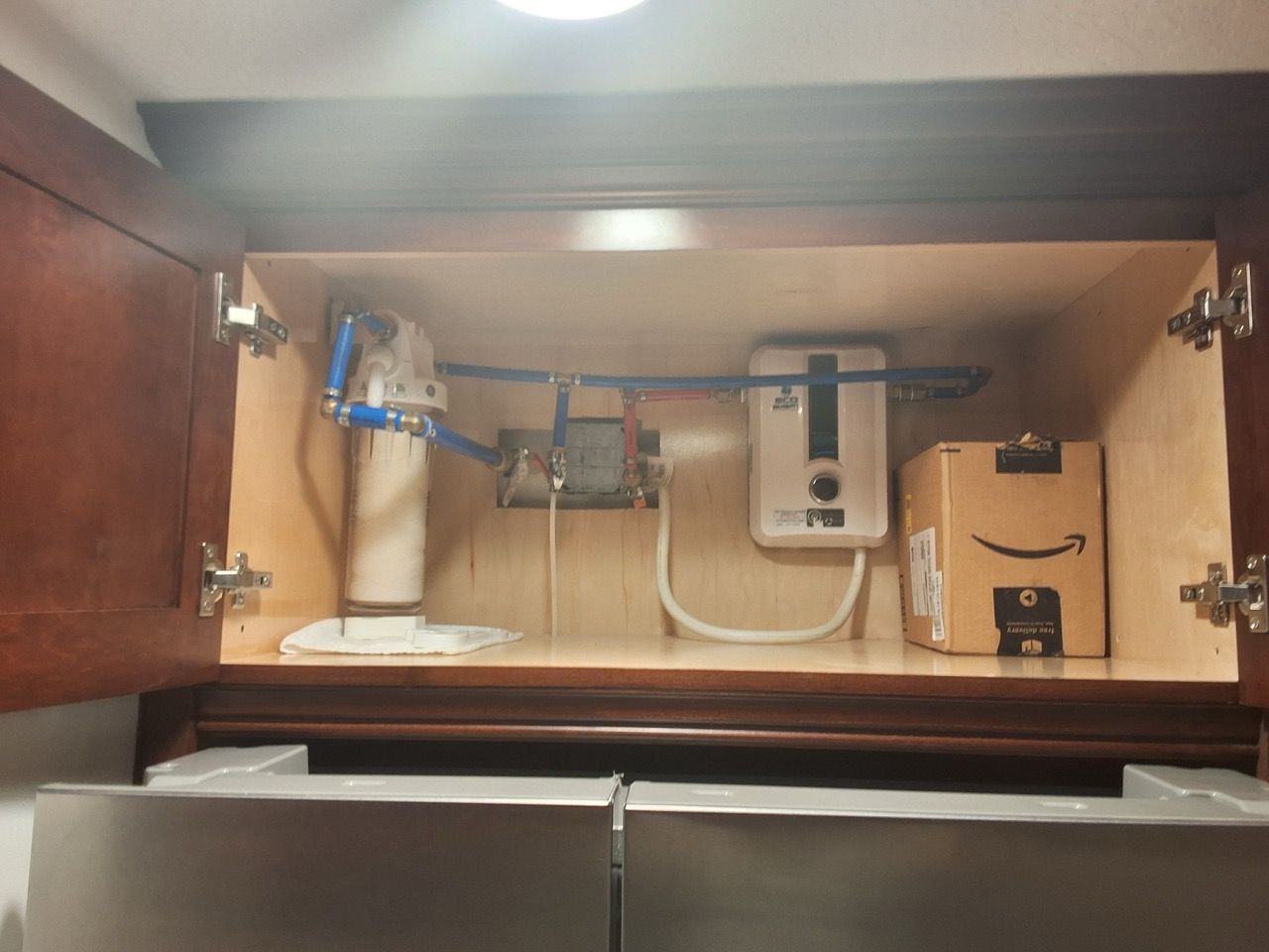 Under-sink cabinet with plumbing, pipes, and a water filter system inside.