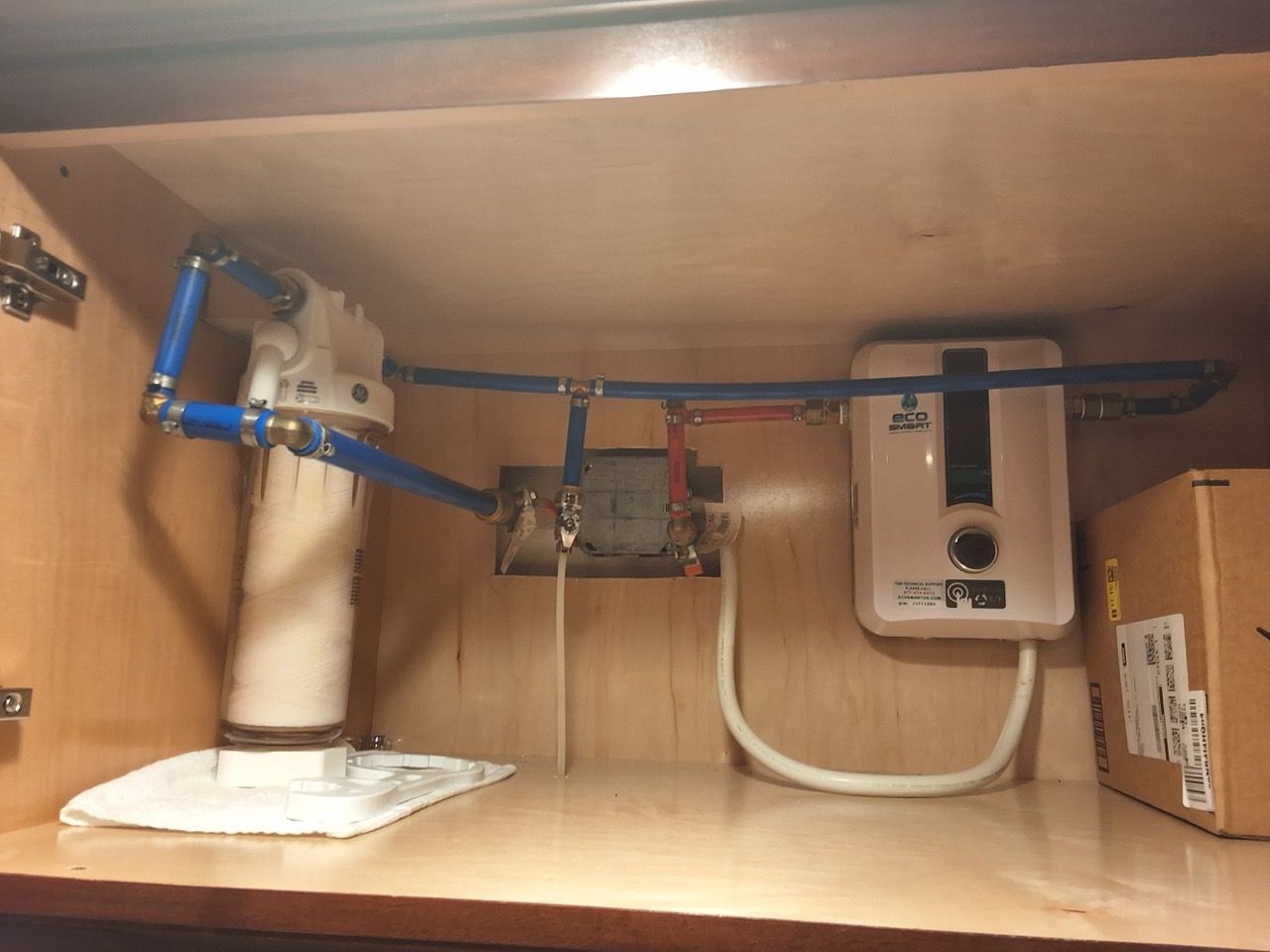 Under-sink plumbing with blue pipes, a pump, and a white water heater inside a cabinet