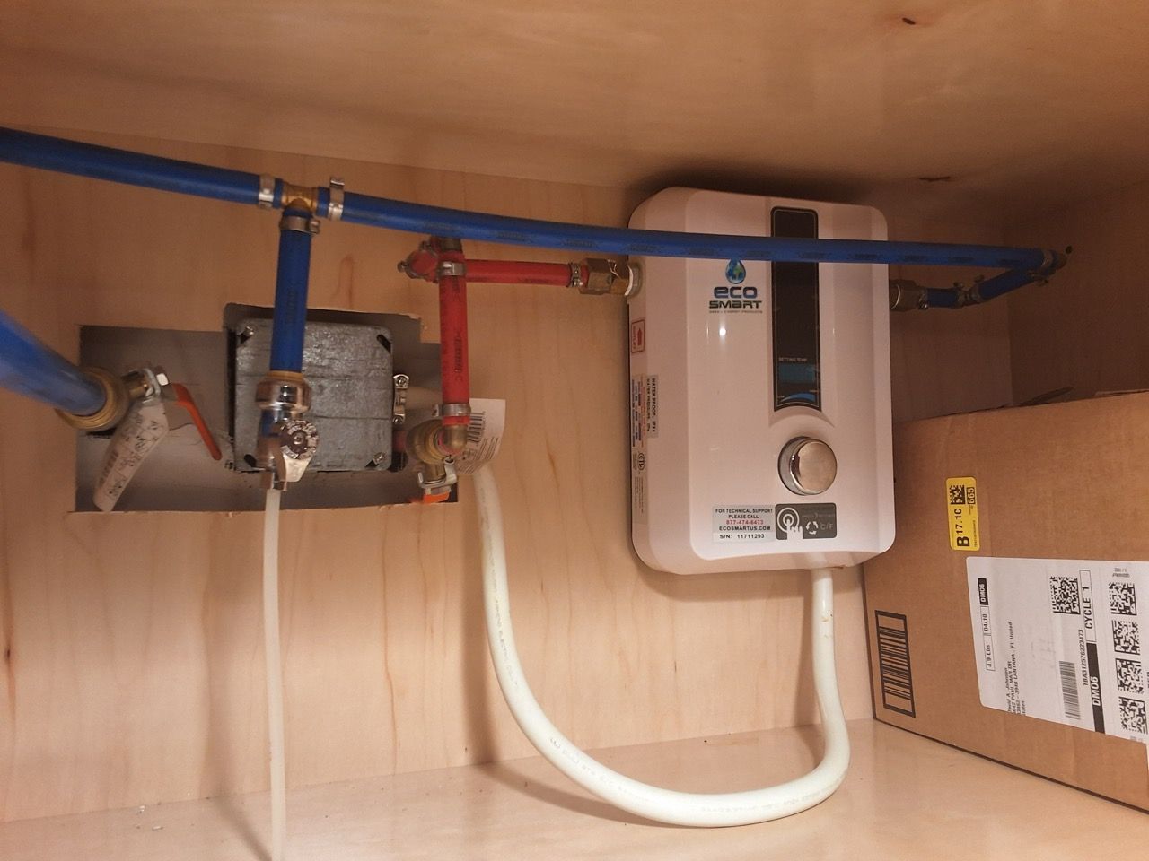 Under-sink plumbing with blue and red shutoff valves and a white water heater mounted inside a cabinet