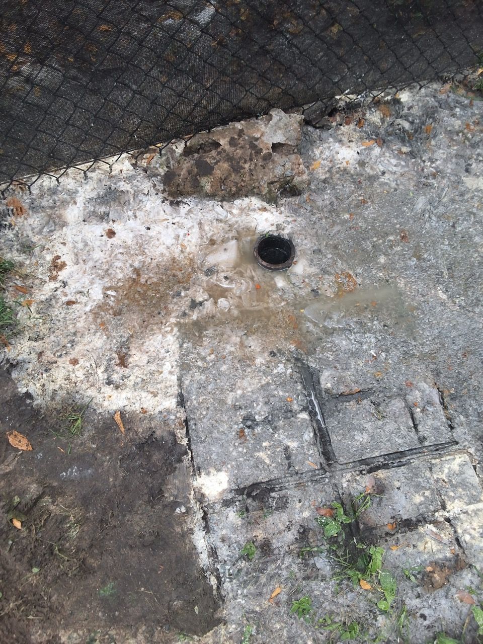 Close-up of a worn concrete surface with a small black drain hole and dirt stains.
