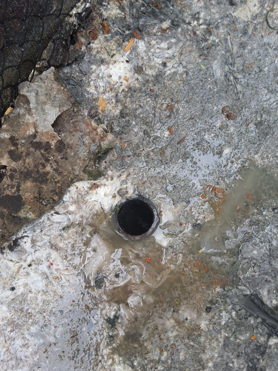 Close-up of a weathered concrete surface with a small circular drain hole and dark stains.