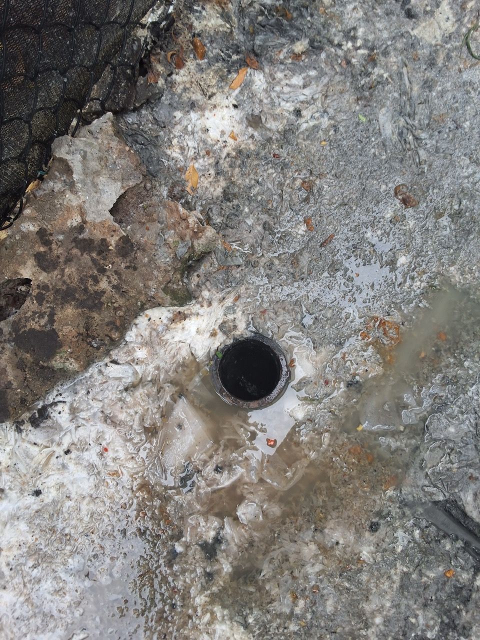 Rusty metal surface with a small round hole near the center, surrounded by weathered gray and brown stains