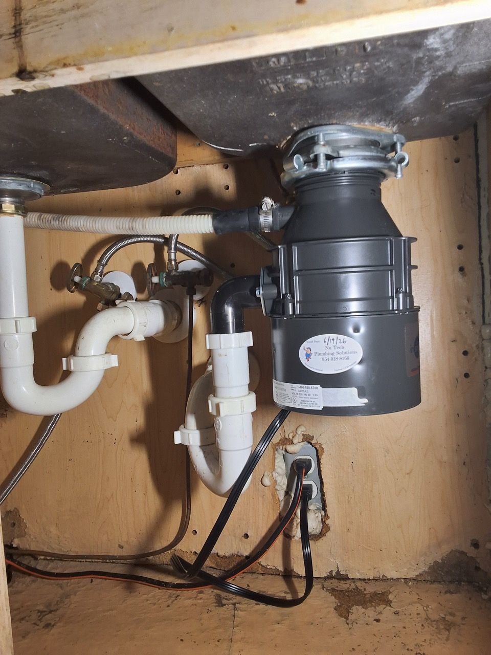 Under-sink garbage disposal and plumbing inside a wooden cabinet