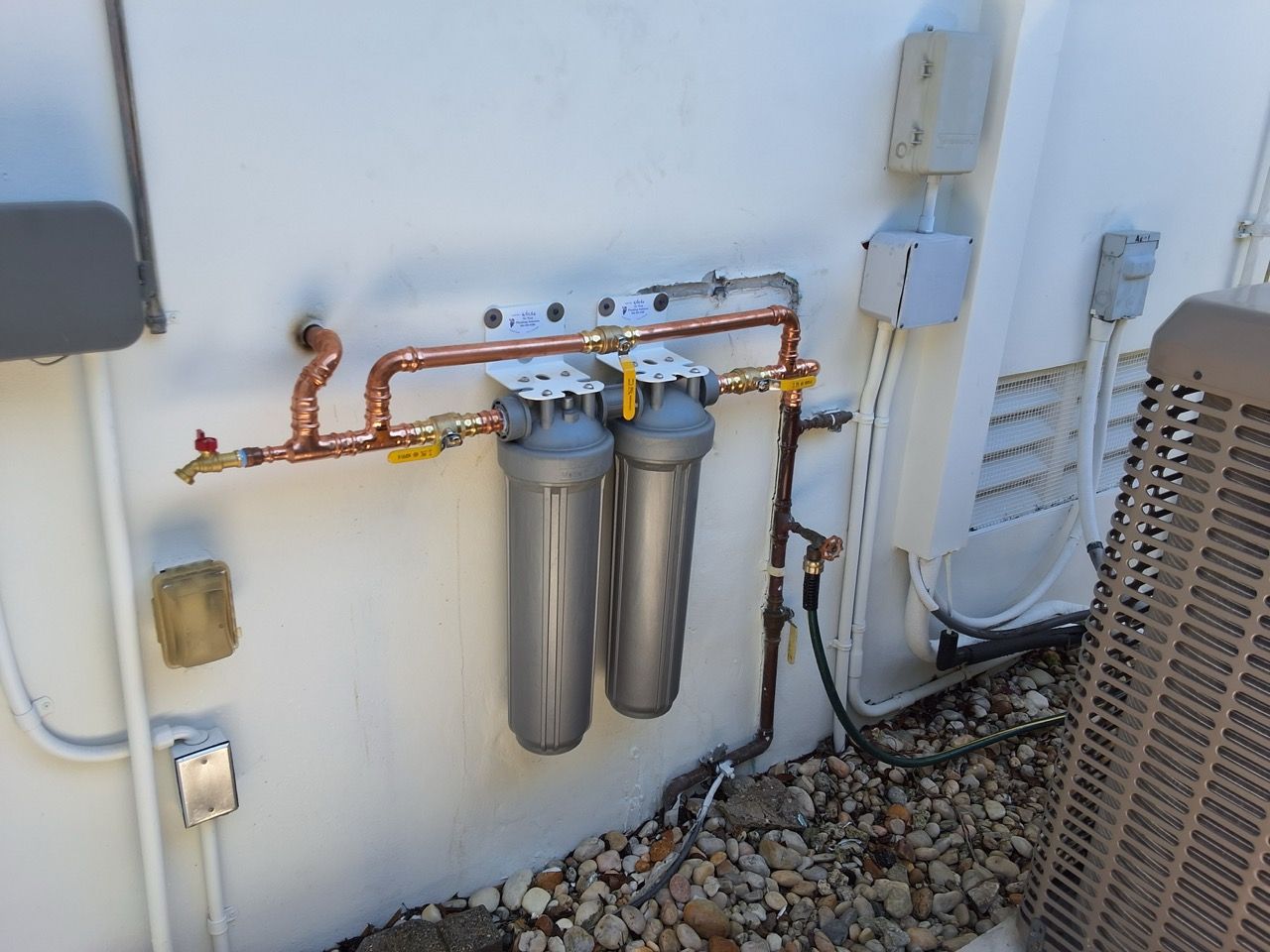 Outdoor wall-mounted water filtration system with copper pipes and two silver filter tanks