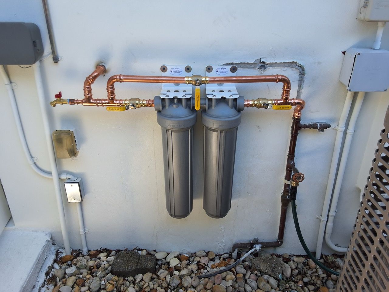 Two water filtration canisters and copper plumbing mounted on an exterior wall