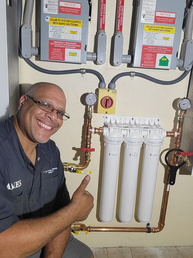 Plumber smiling and pointing at a water filtration system with pipes and valves in a utility room