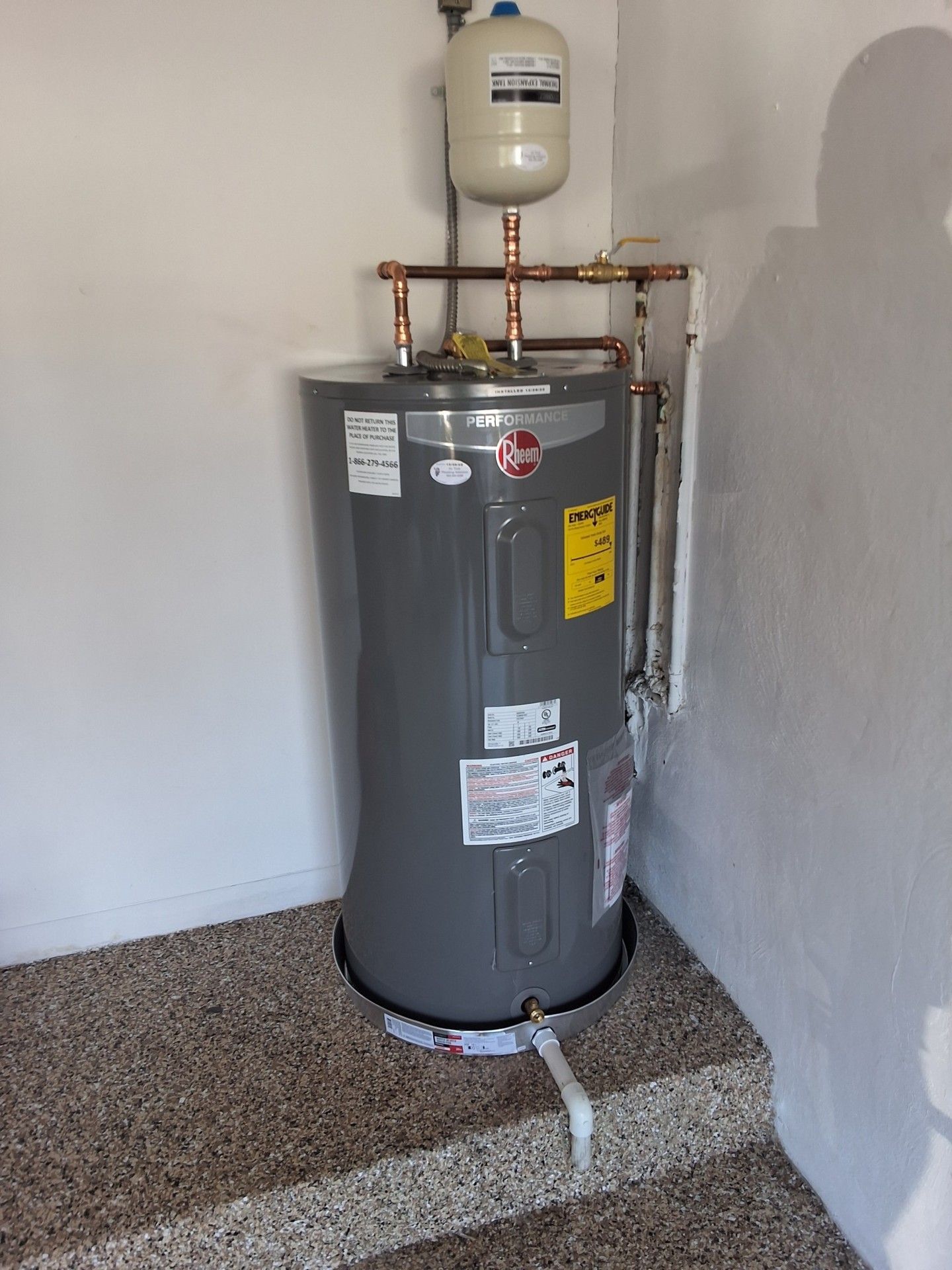 Water heater with expansion tank and copper pipes in a garage-like utility room.