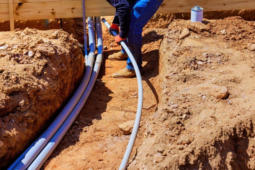 Worker installing white utility pipes in a dirt trench at a construction site