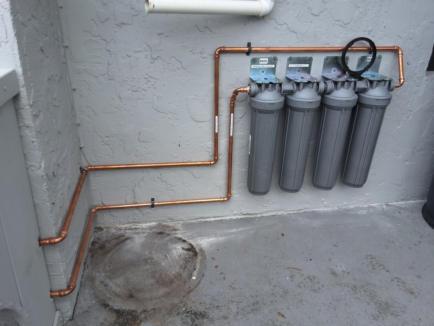 Copper pipes and four gray filters mounted on a concrete wall in an industrial utility area