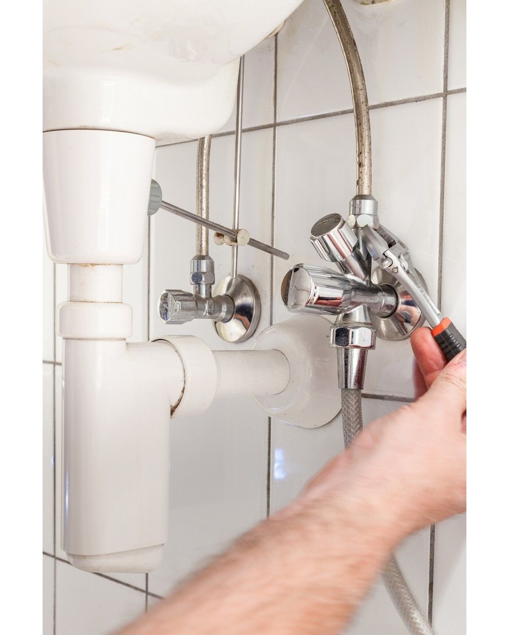 Plumber tightening a bathroom sink supply valve with a wrench under a tiled wall