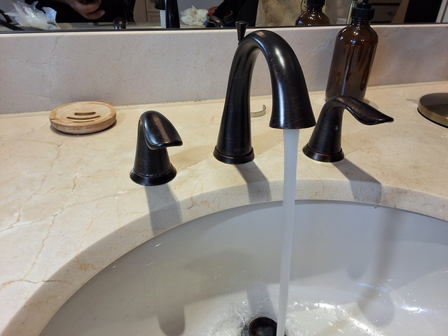 Black faucet running water into a white bathroom sink with a curved counter.