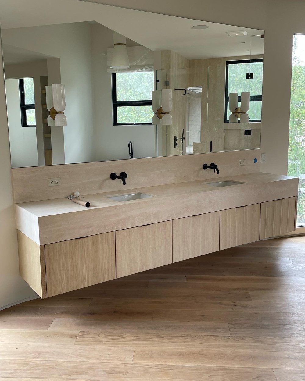Modern bathroom vanity with double sinks, large mirror, and wood cabinetry in a bright room