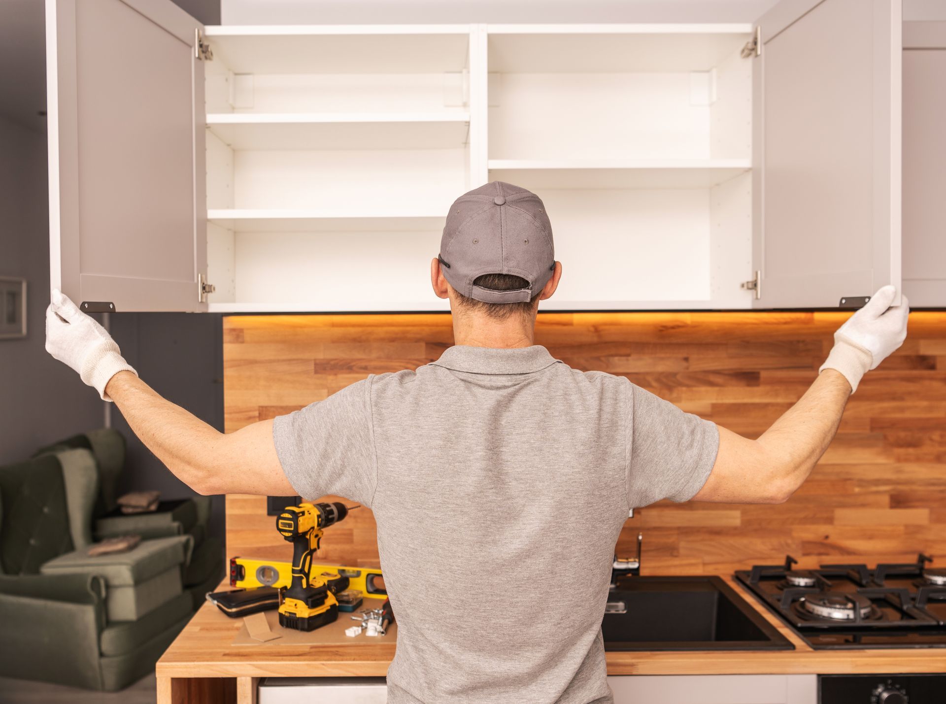 Person installing white kitchen cabinets above a wood backsplash, viewed from behind.