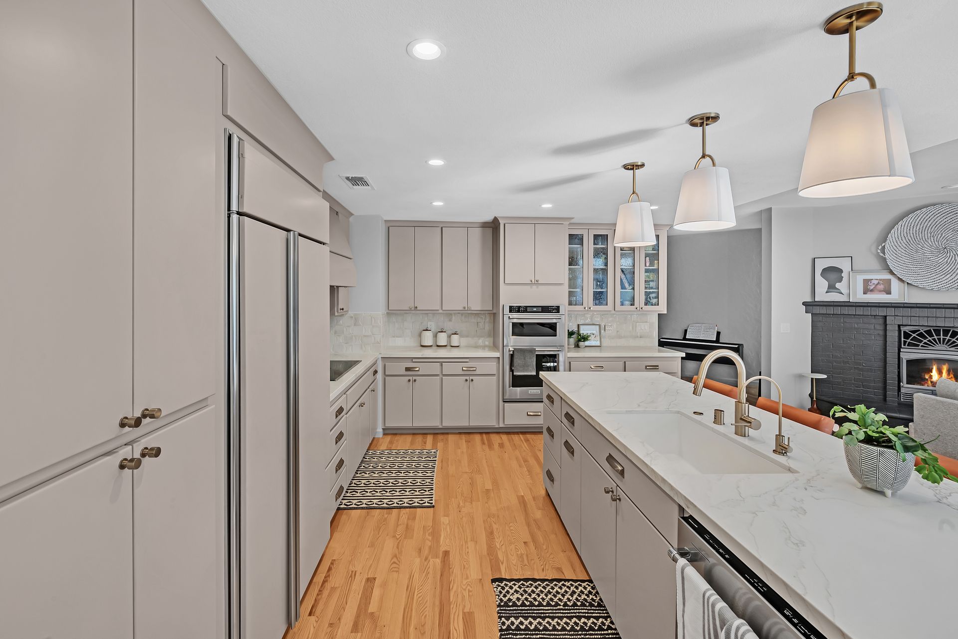 Modern white kitchen with island, stainless appliances, pendant lights, and wood floors