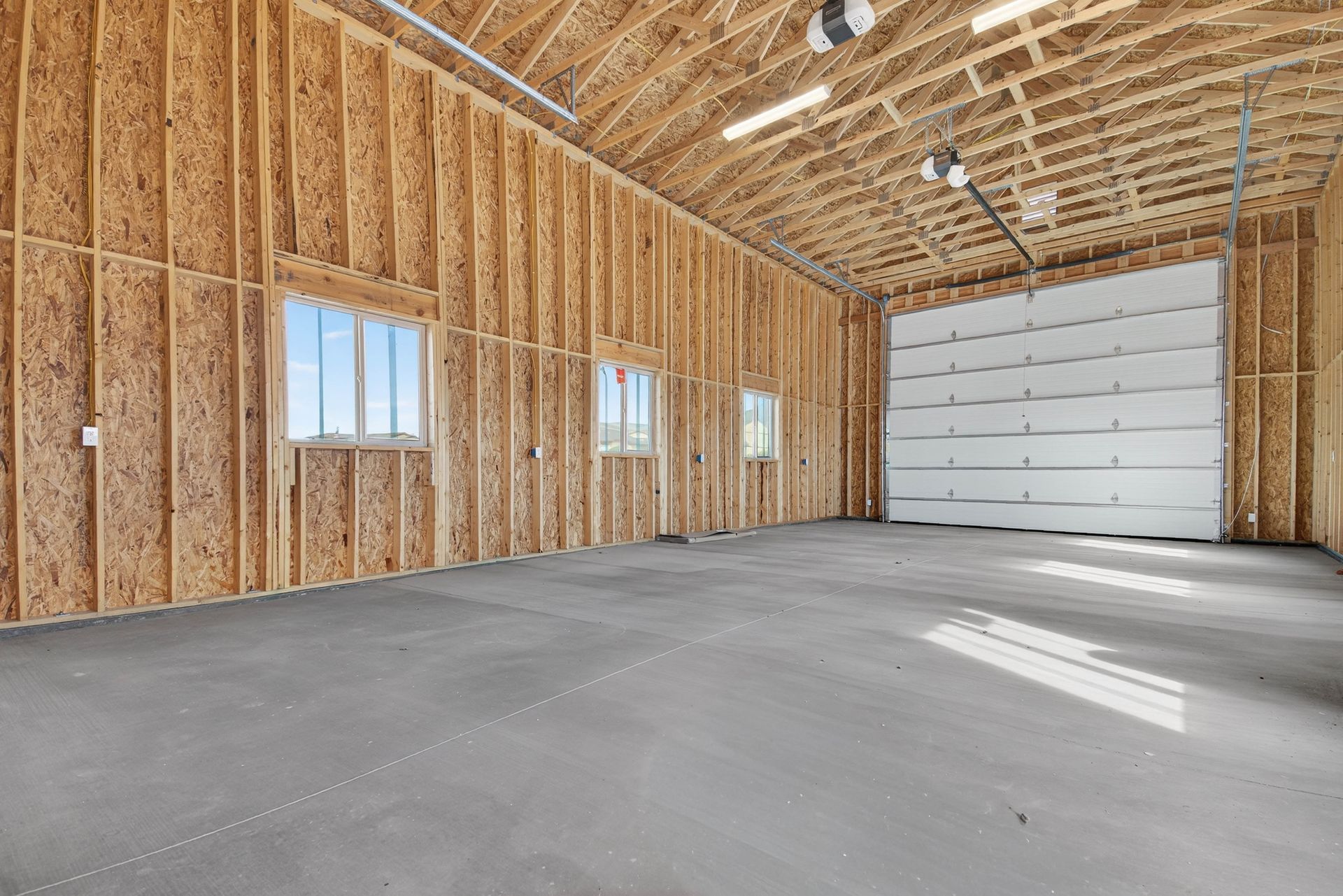 Empty unfinished garage with wood framing, concrete floor, and a large white overhead door