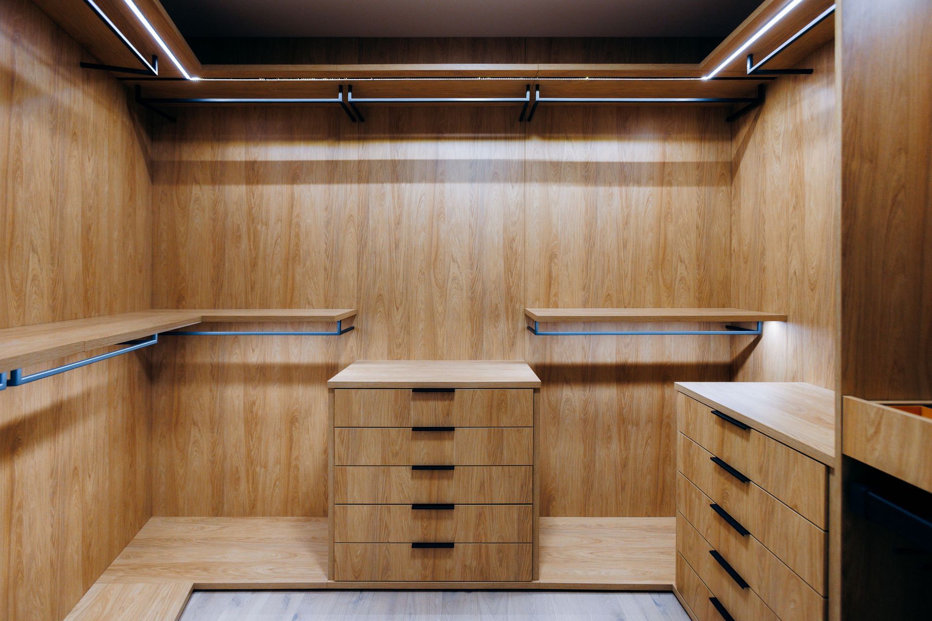 Wood-paneled walk-in closet with shelves, hanging rods, and drawers under warm lighting