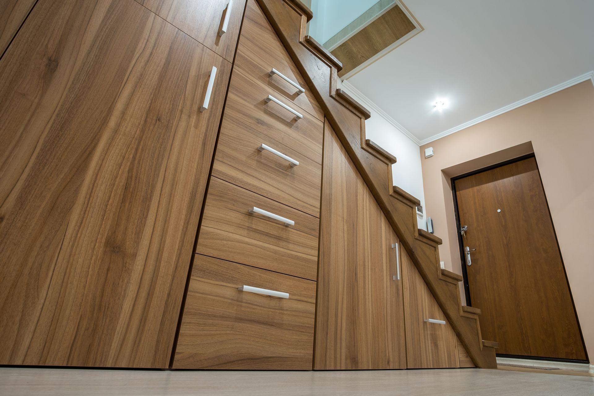 Wooden built-in cabinets and staircase in a modern hallway, with a closed door at the end.