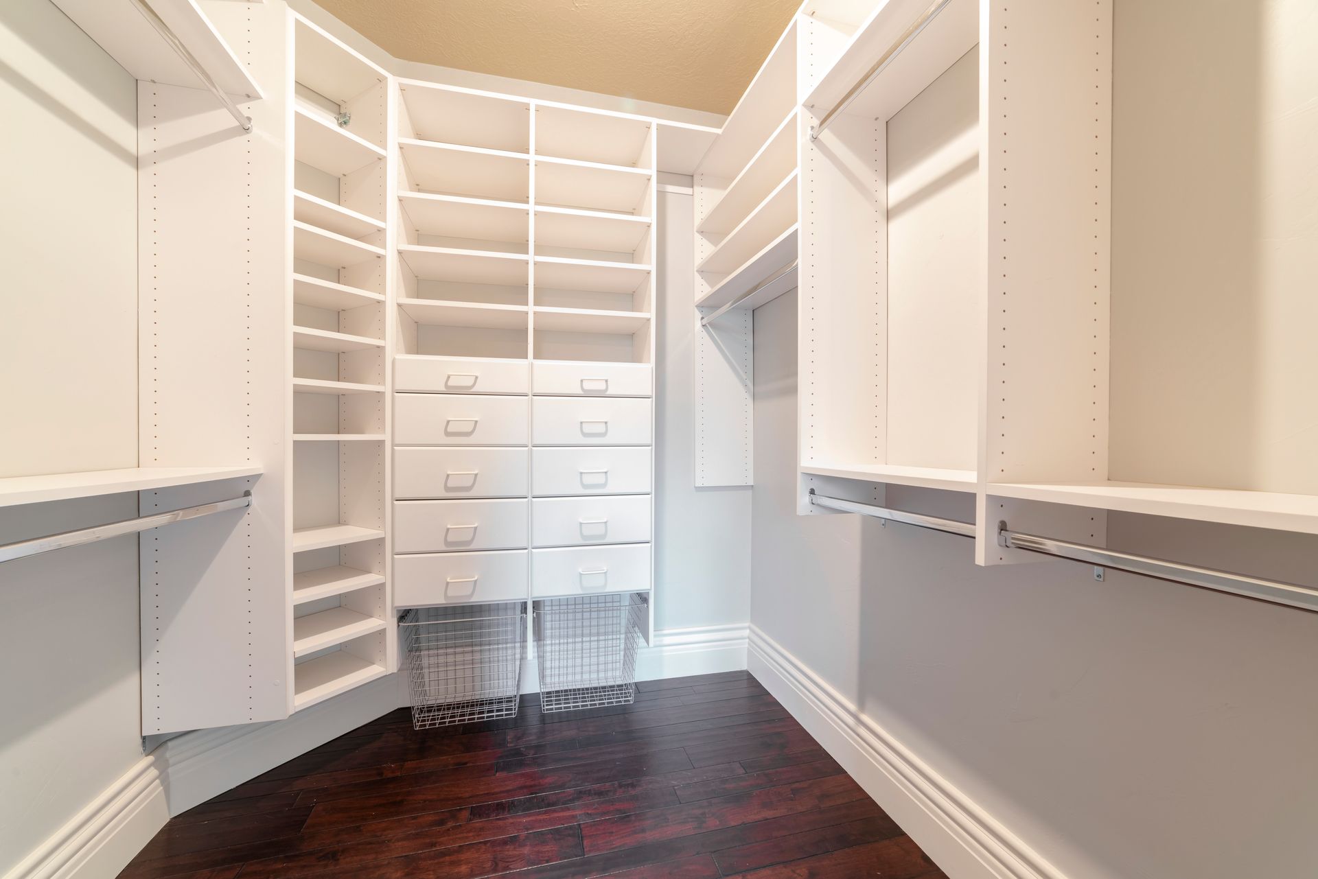 Spacious white walk-in closet with shelves, drawers, and hanging rods, dark wood floor.