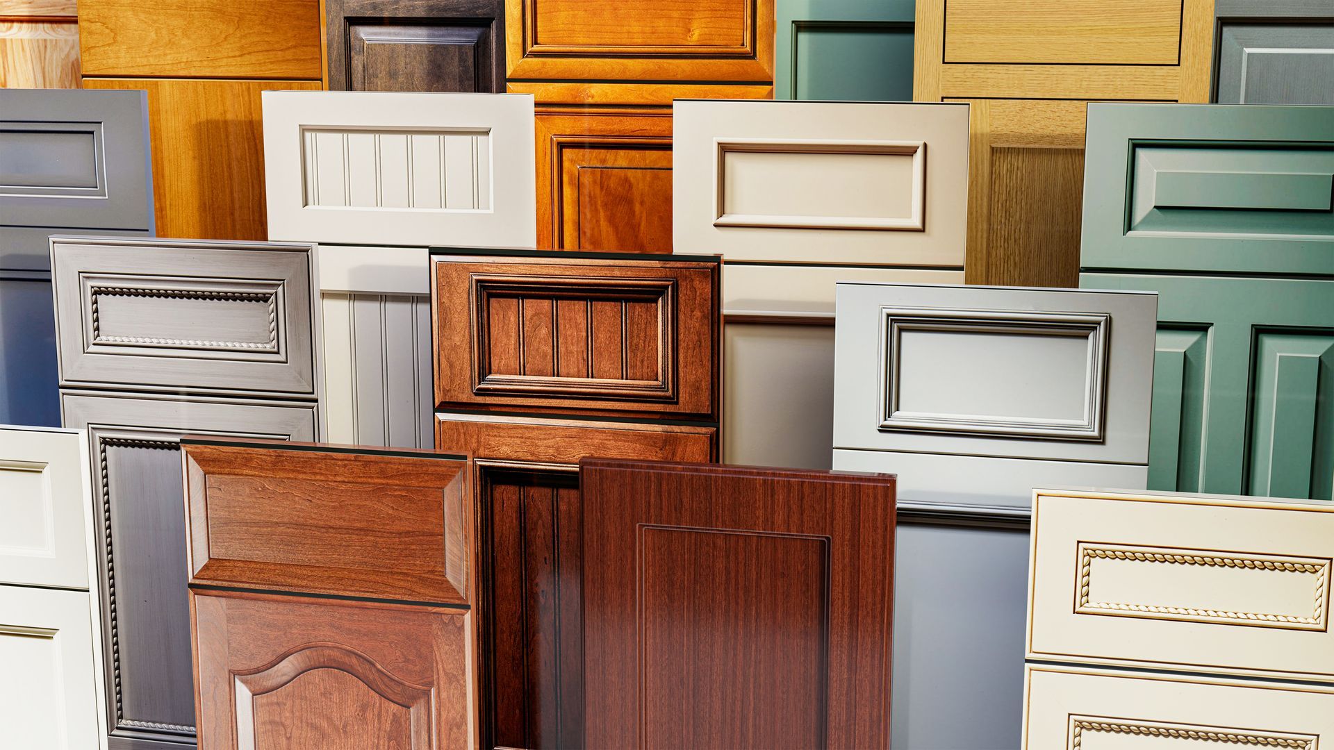Assorted wooden cabinet doors and drawer fronts stacked in overlapping rows, in white, wood, and teal tones
