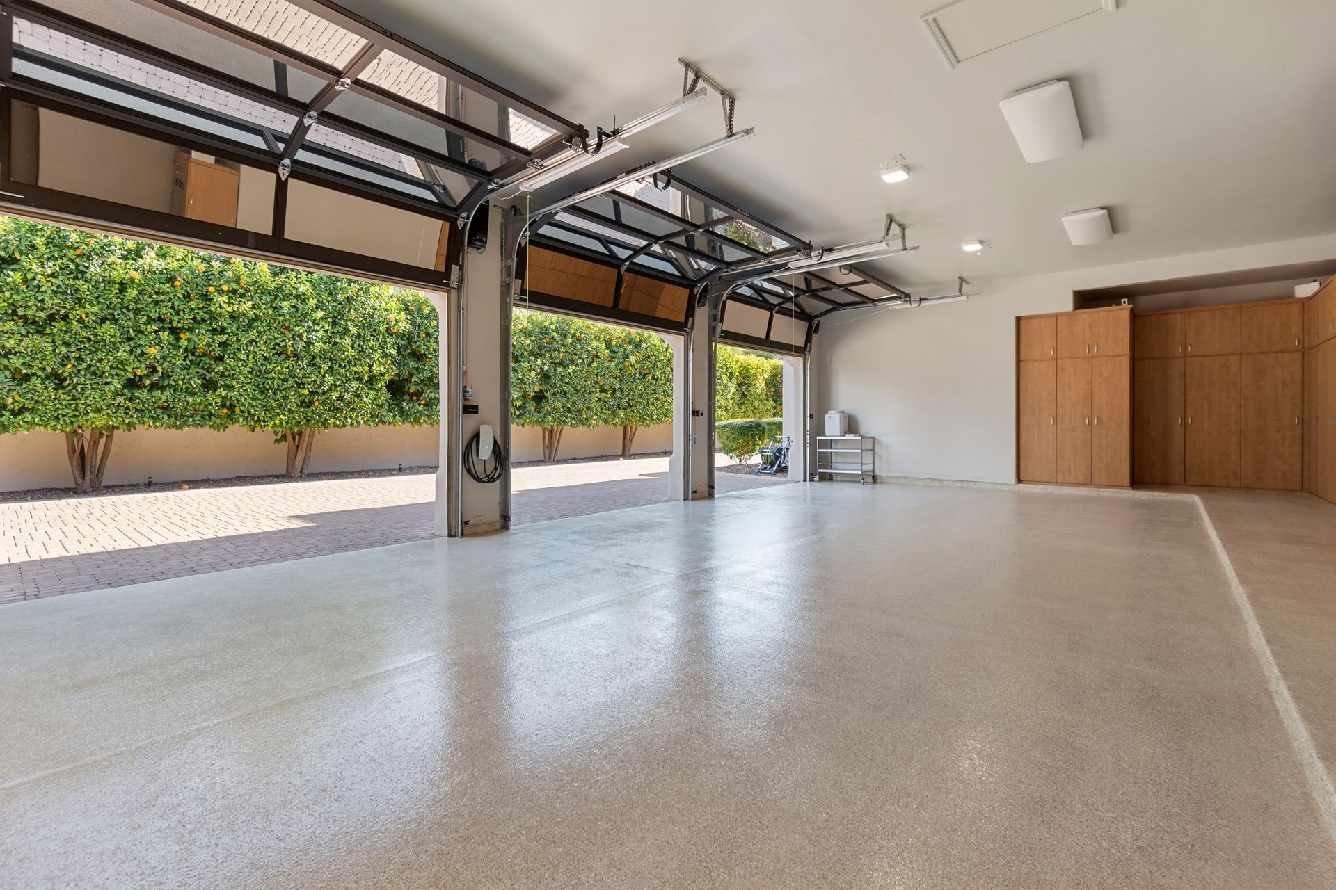 Empty modern garage with open doors, white floor, and wooden storage cabinets along the wall