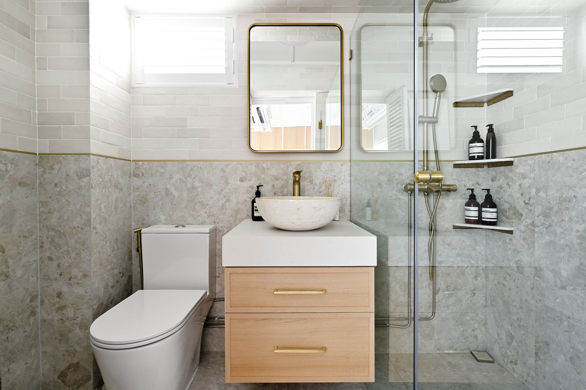 Modern bathroom with toilet, vanity sink, glass shower, and gray tile walls
