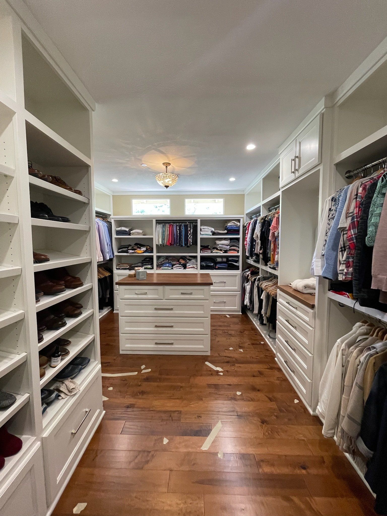 Walk-in closet with white shelves, hanging clothes, and a central island on a wooden floor
