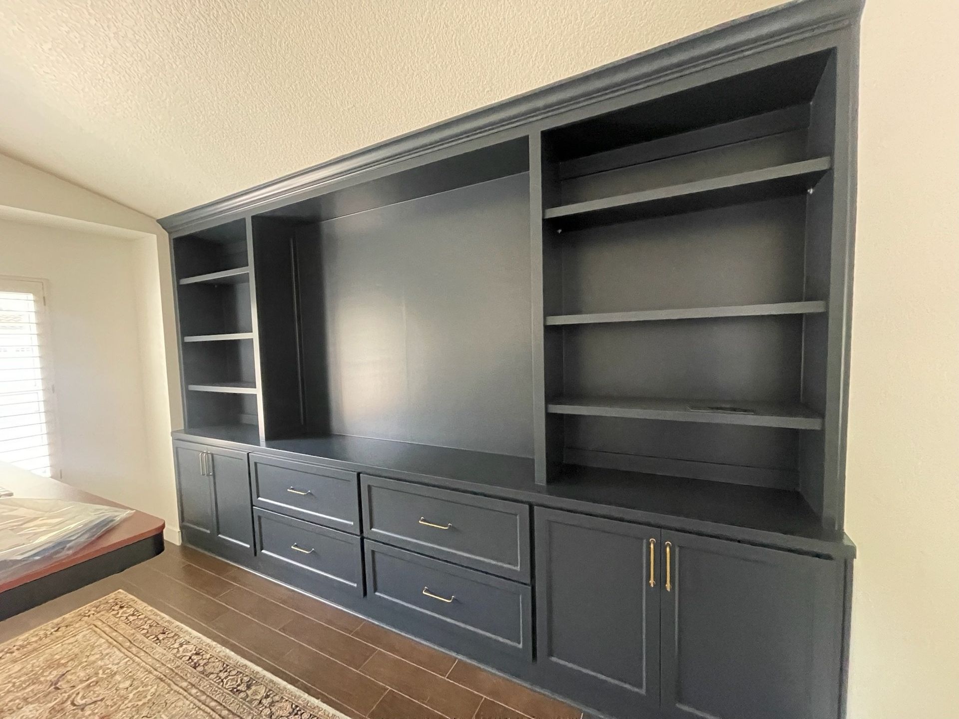 Built-in dark gray entertainment center with shelves, cabinets, and large TV space in a bedroom