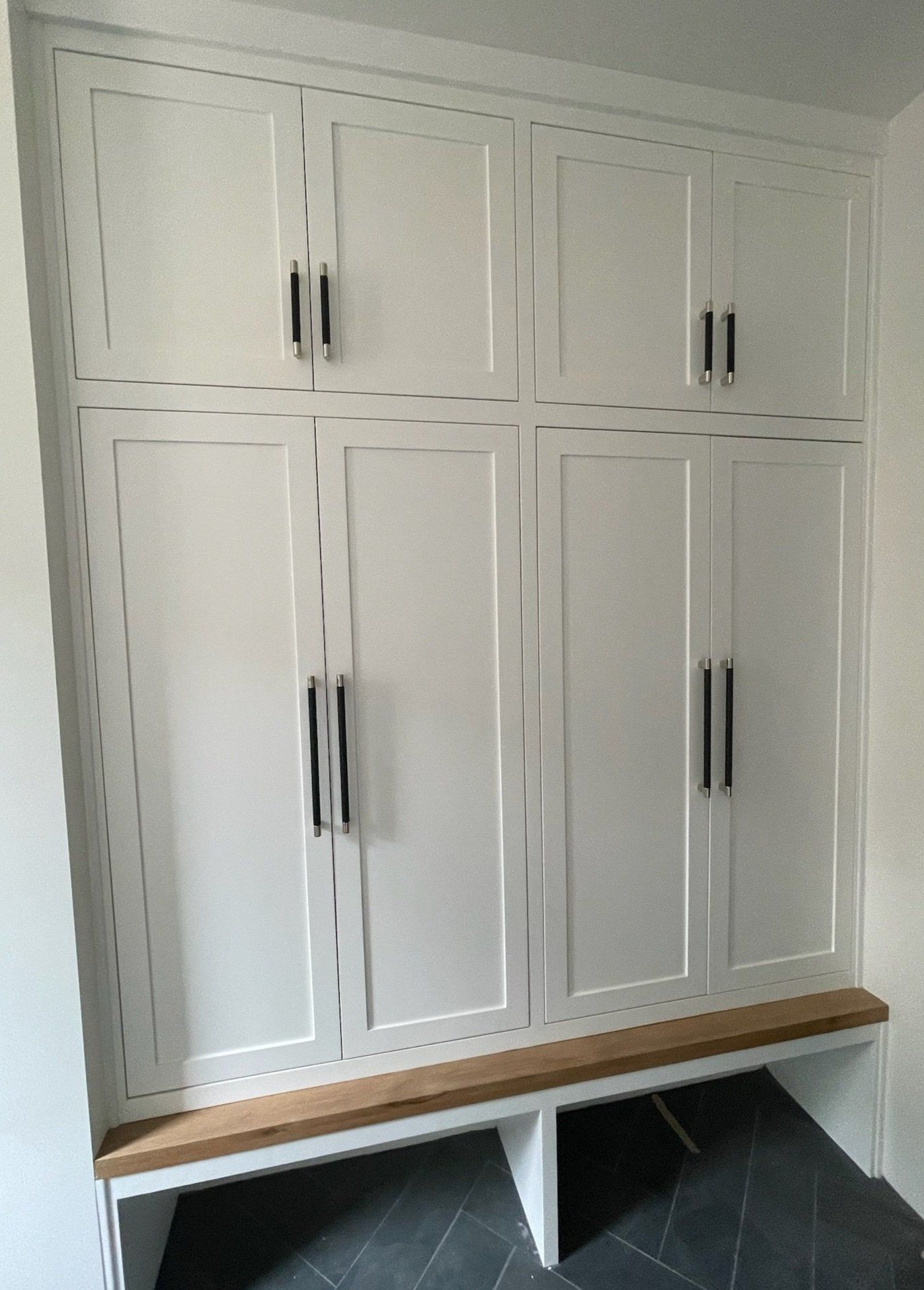 White built-in cabinet with black handles above a wooden bench and two white storage bins underneath.