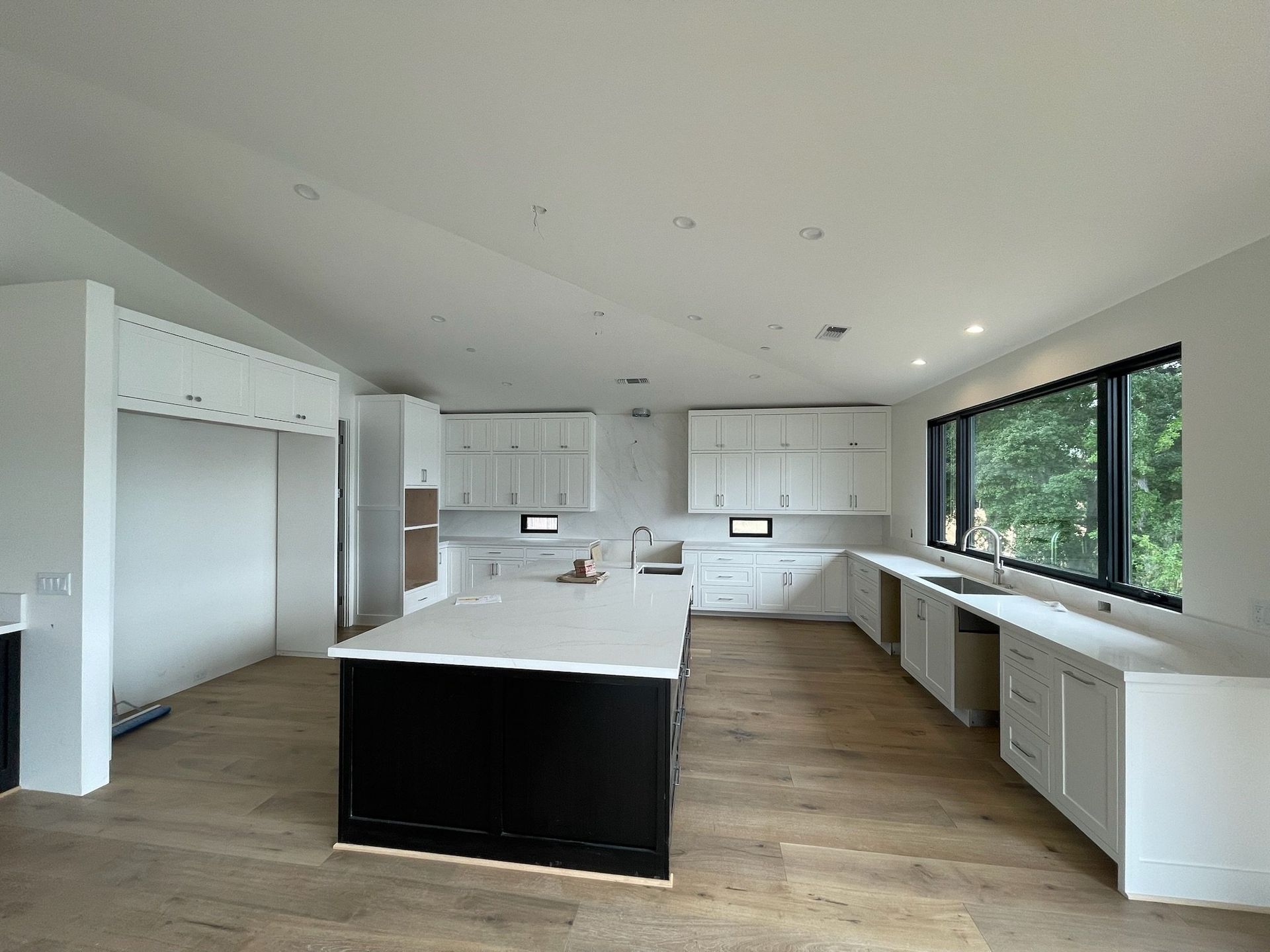 Bright modern kitchen with white cabinets, large island, wood floors, and big windows overlooking trees