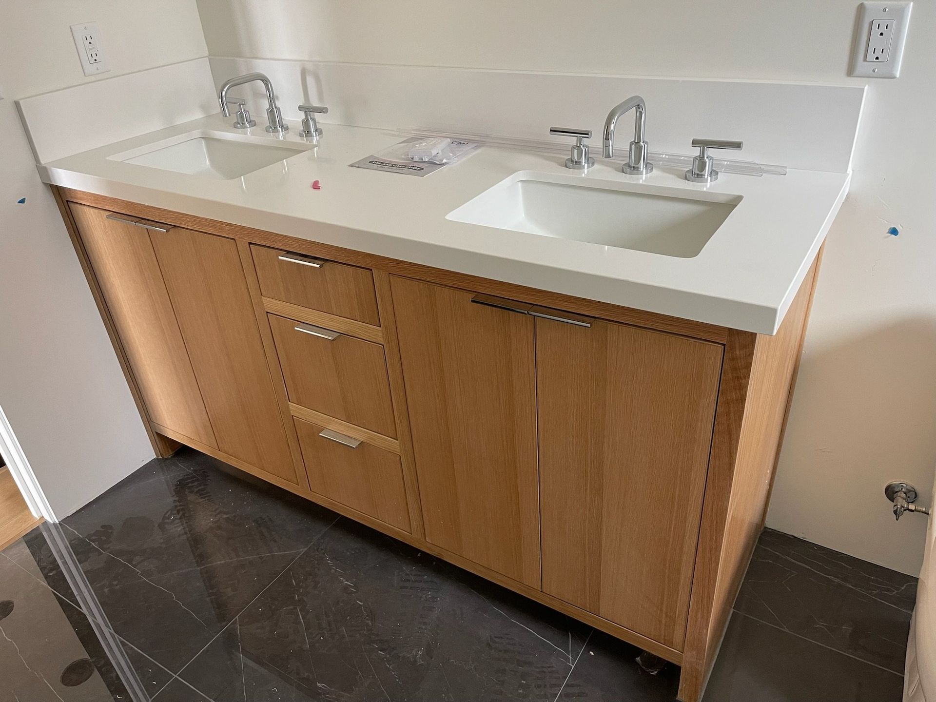Wooden bathroom vanity with white countertop and sink, mirror above, and dark tile floor