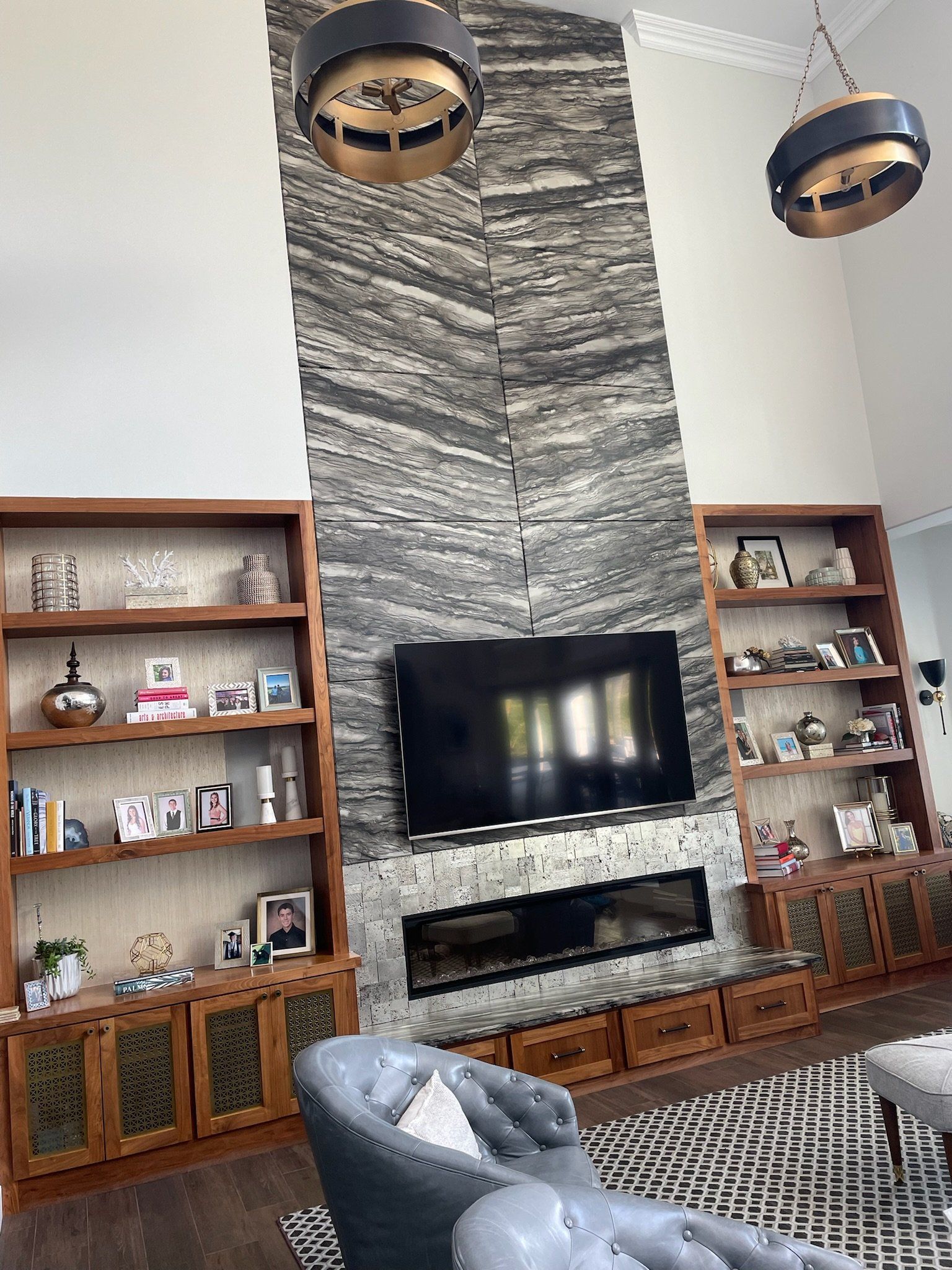 Living room with stone fireplace, TV, wooden shelves, and two pendant lights above a patterned rug