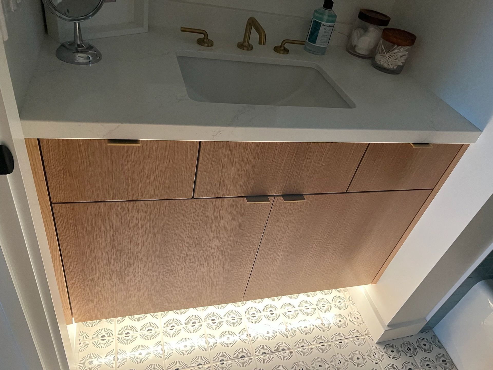 Bathroom vanity with sink, wood cabinet doors, and under-cabinet lighting