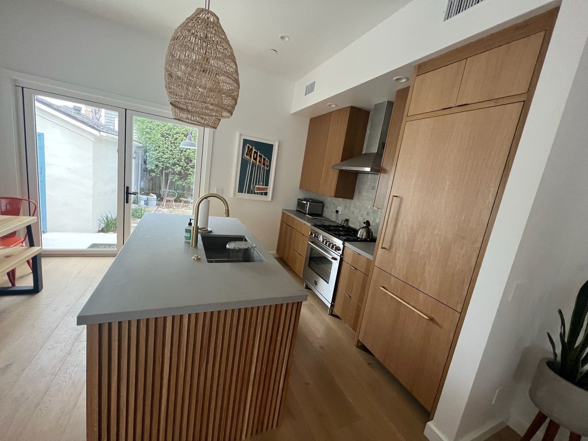Bright modern kitchen with wood cabinets, island, pendant light, and open doors to a patio.