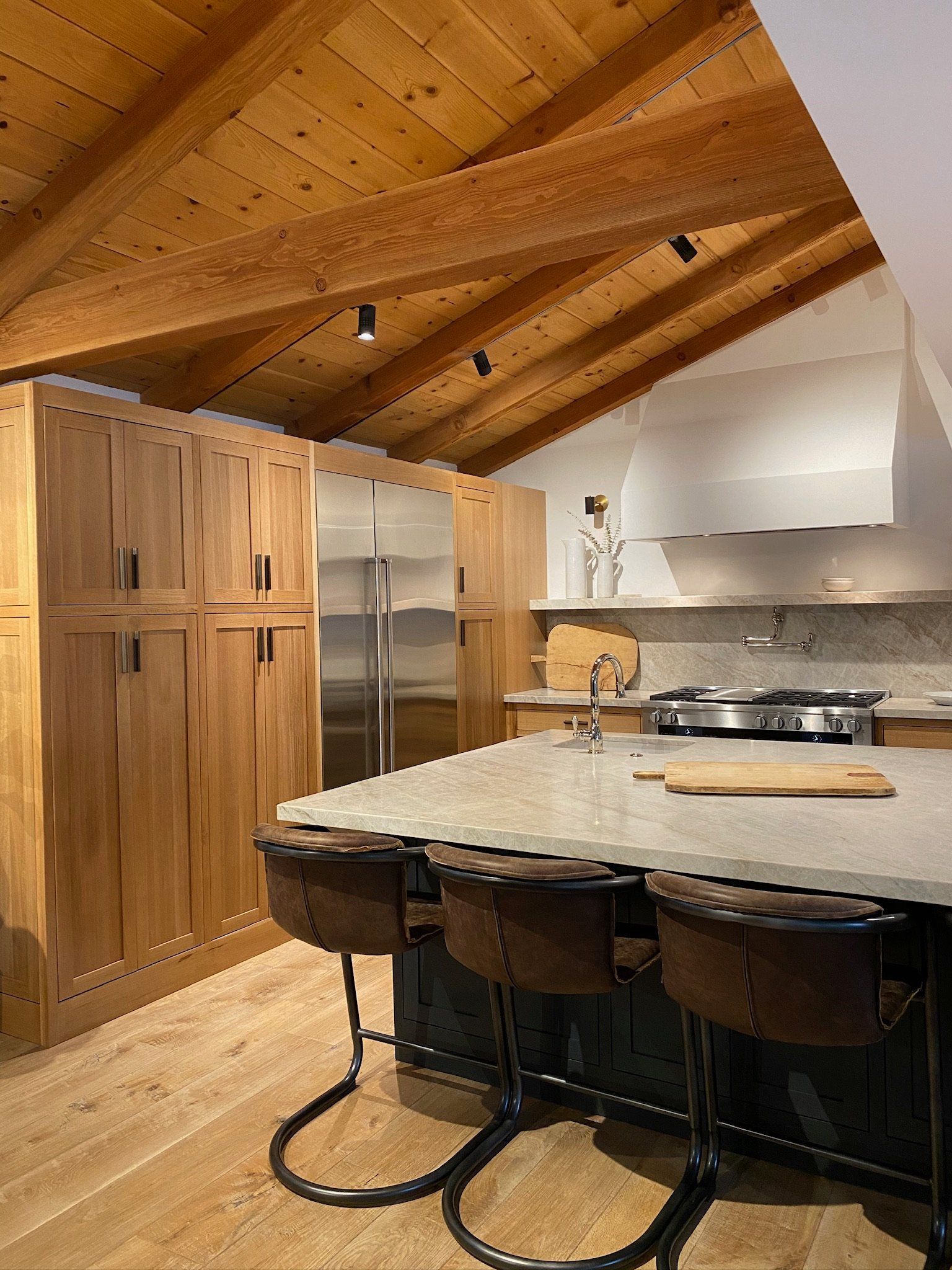 Modern kitchen with wood-paneled ceiling, stainless appliances, island stools, and a granite countertop