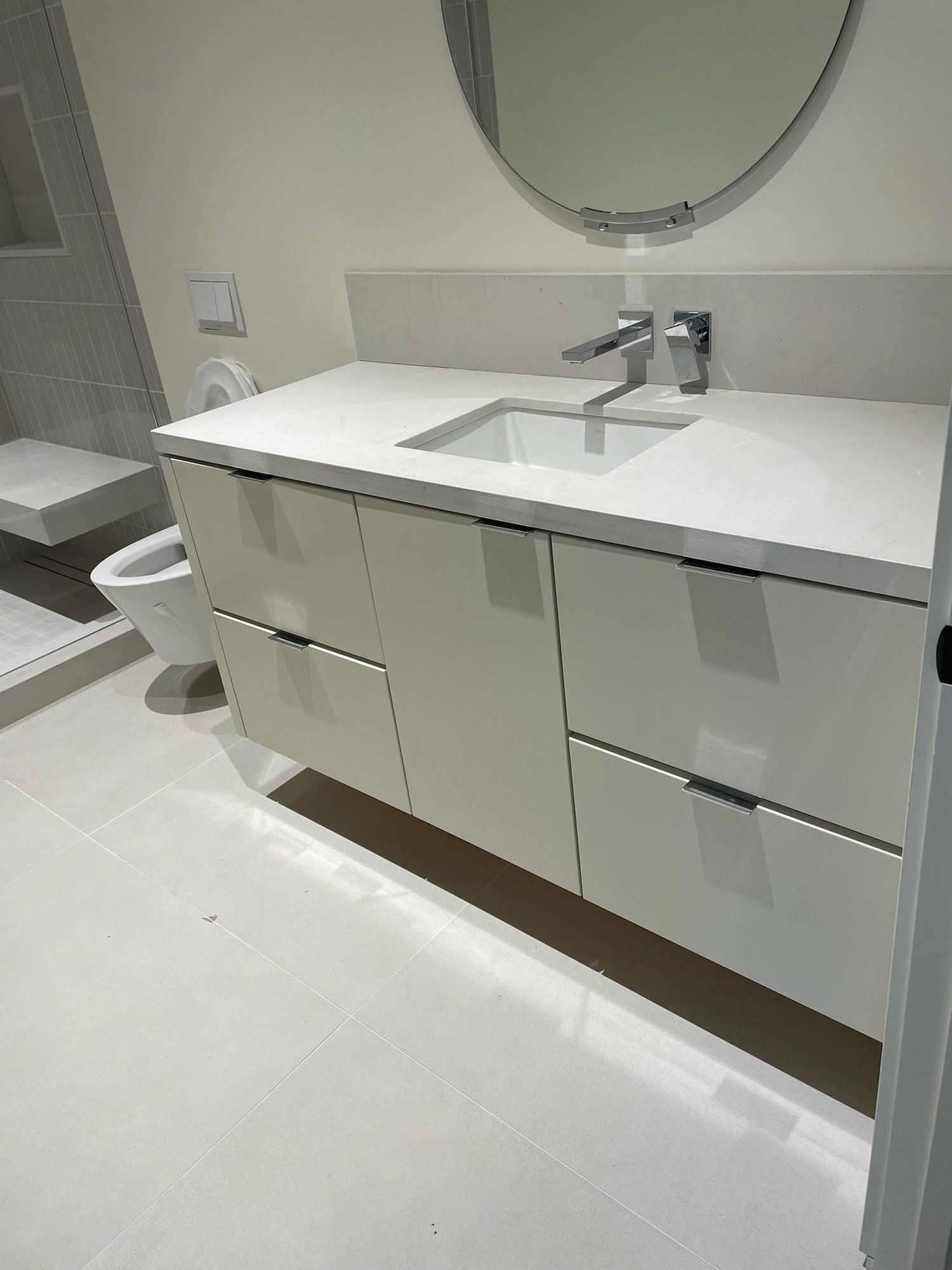 Modern bathroom vanity with white countertop, chrome faucet, oval mirror, and built-in drawers.