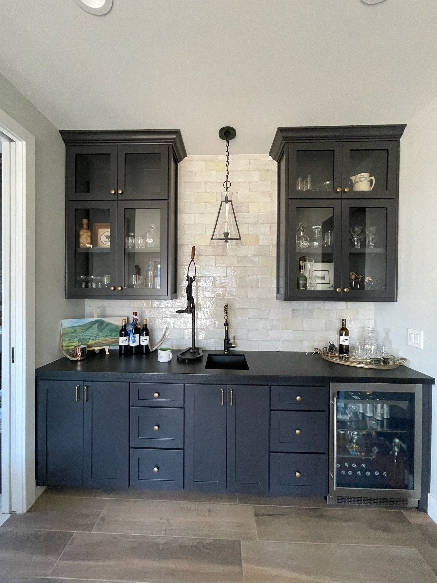 Modern kitchen with dark cabinets, glass-front upper cupboards, and a white tiled backsplash.